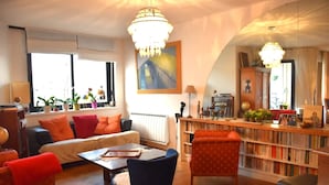 Ein gemütliches Wohnzimmer mit einer Couch, Sesseln, einem Couchtisch und einem Bücherregal voller Bücher.