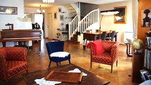 Ein Wohnzimmer mit einem Flügel, einem blauen Sessel, einem roten Sofa und einem Holztisch.