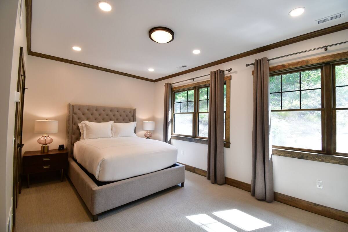 A bedroom with a large bed, a nightstand, a window with curtains, and a ceiling light.