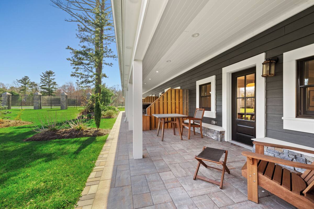 A covered patio with outdoor furniture, a stone pathway, and a view of a grassy area.