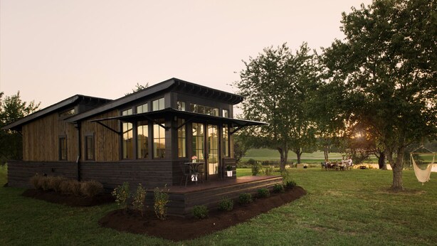 A modern wooden cabin with a glass front, a deck, and a view of a grassy field and trees. - The Preserve Sporting Club & Resort (Richmond)