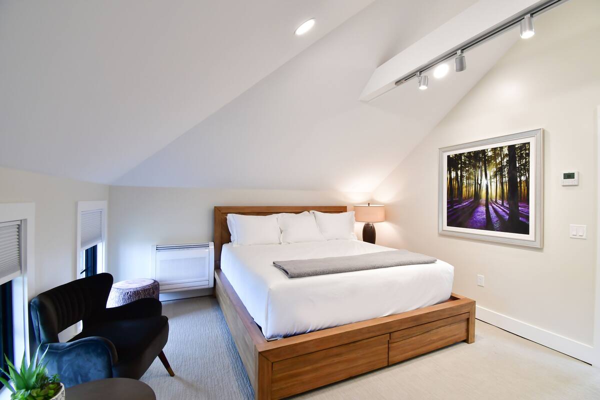 A modern bedroom with a large bed, a chair, a small table, and a painting on the wall.