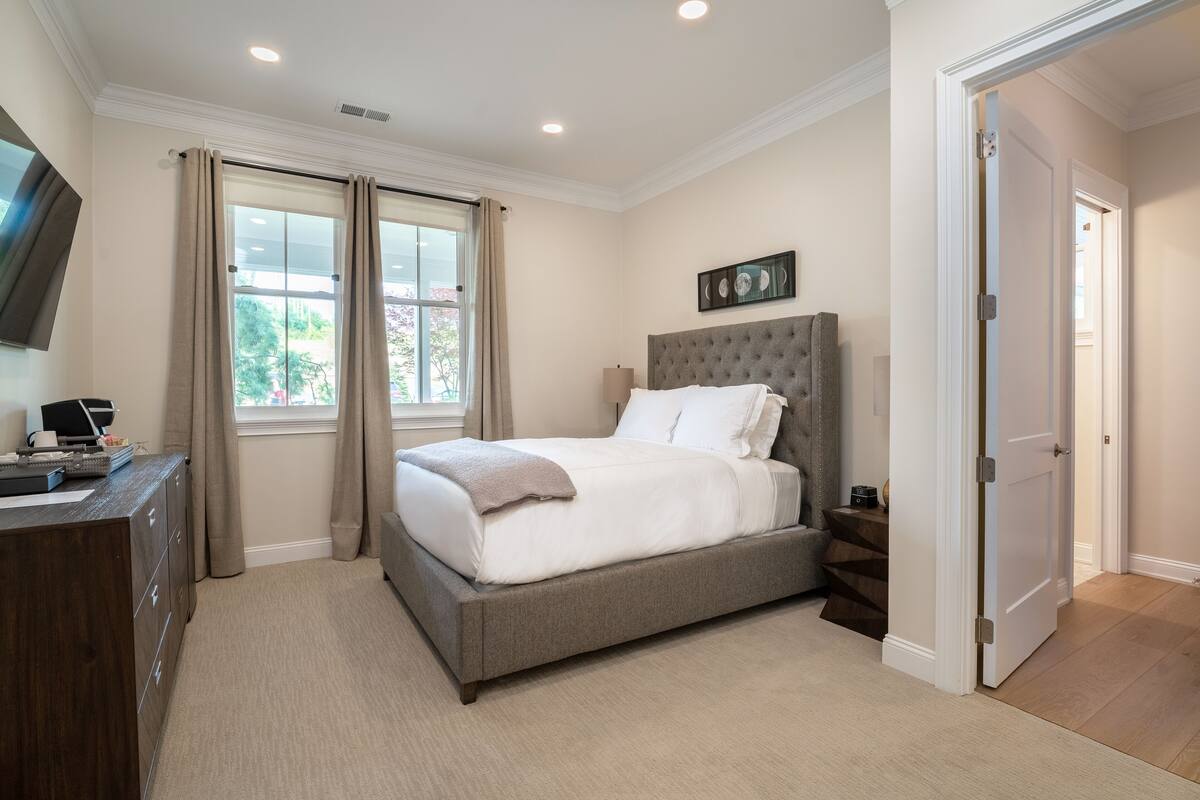 A bedroom with a large bed, a dresser, a TV, and a window with curtains.