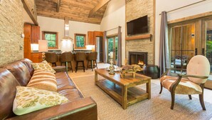 A spacious living room with a leather couch, wooden coffee table, and a fireplace. There are multiple seating areas and a large window providing natural light. - The Preserve Sporting Club & Resort (Richmond)