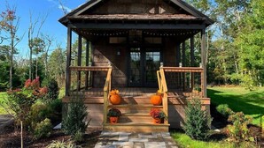 A rustic cabin with a wooden porch, steps leading to a door, and decorative pumpkins. - The Preserve Sporting Club & Resort (Richmond)