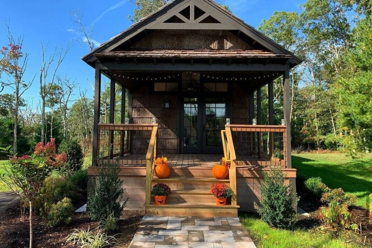 A rustic cabin with a wooden porch, steps leading to a door, and decorative pumpkins.