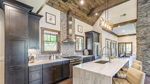 A spacious kitchen with dark cabinetry, a large island, and a stone accent wall. - The Preserve Sporting Club & Resort (Richmond)