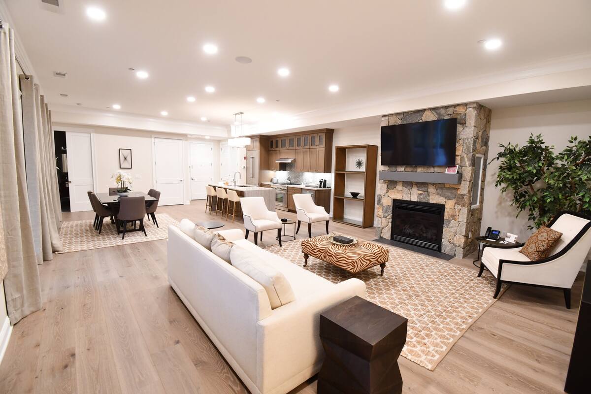 A spacious living area with a sofa, chairs, a fireplace, a TV, and a kitchen in the background.