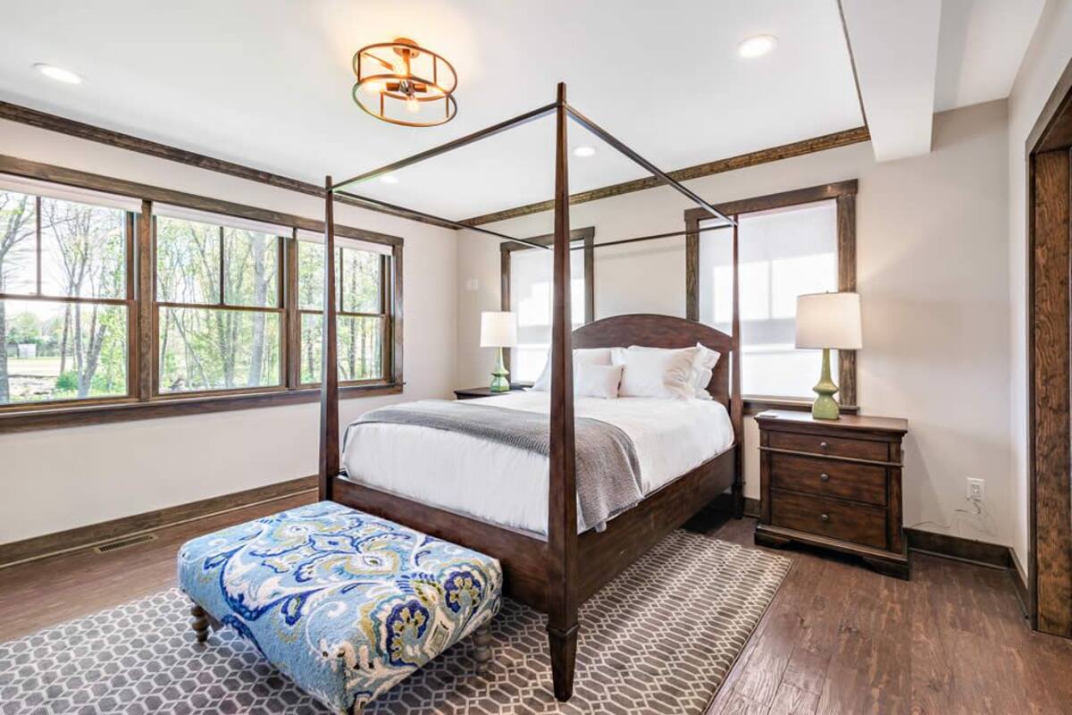 A four-poster bed with a wooden frame, a matching bench, and a nightstand with a lamp.