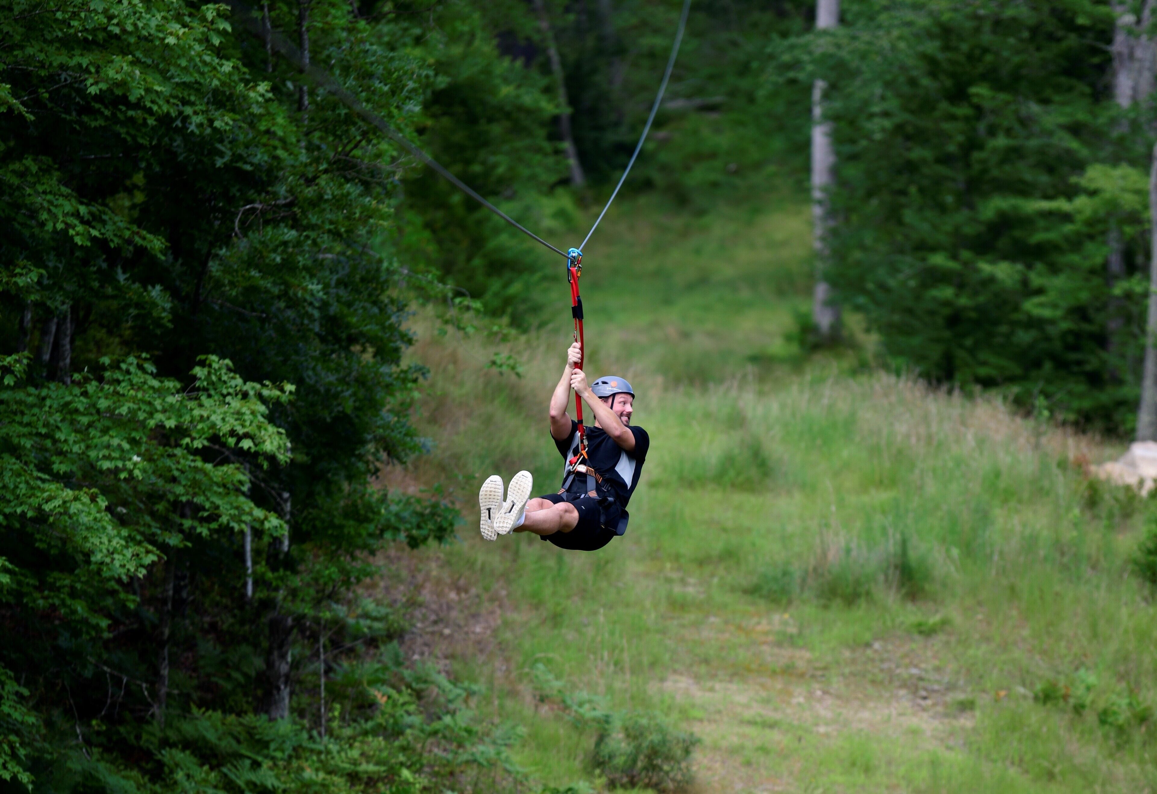 A person suspended in mid-air, likely engaging in an outdoor activity such as zip-lining or paragliding, surrounded by dense green foliage.
