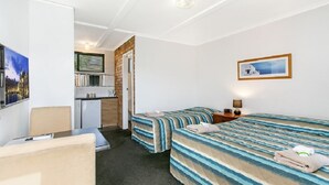 Habitación de hotel con dos camas, un escritorio, una silla, kitchenette y baño.
