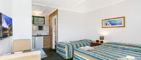 A hotel room with two beds, a desk, a chair, a kitchenette, and a bathroom.