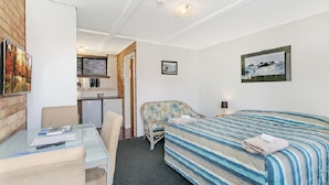 Una habitación de hotel con cama, escritorio, silla, kitchenette y baño.