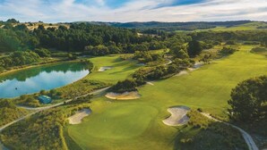 Un campo de golf con un estanque, búnkeres de arena y un club de campo.