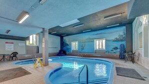 An indoor swimming pool with clear water, two ladders, and a mural of a mountainous landscape on the wall.