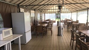 A covered outdoor dining area with tables and chairs, a refrigerator, and a microwave.