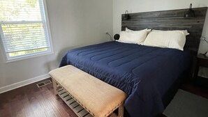 Een slaapkamer met een bed, een houten bankje, een plafondventilator en een raam met zonwering.