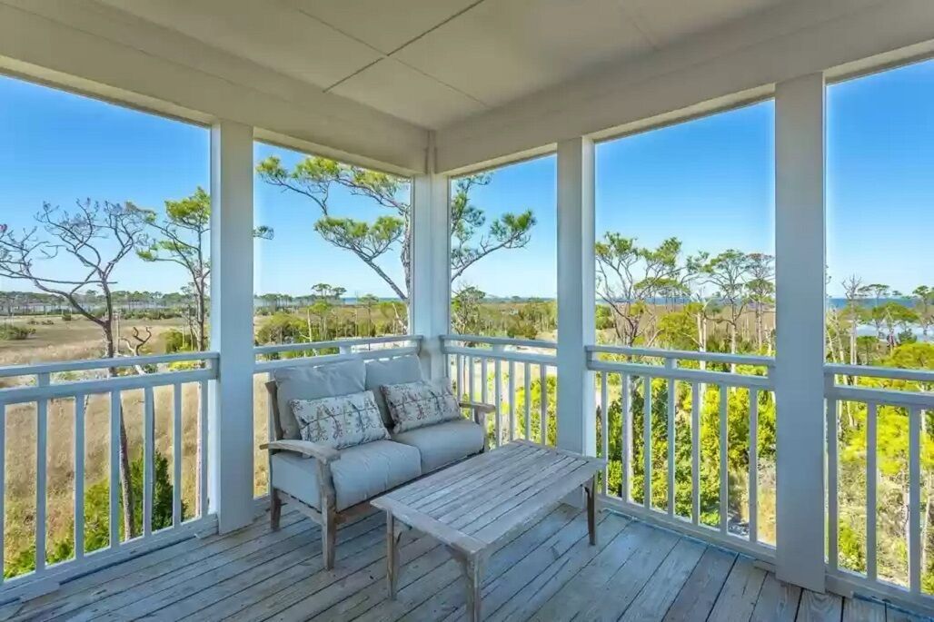 Eine überdachte Veranda mit einer hölzernen Bank und einer Couch, die einen Blick auf eine natürliche Landschaft mit Bäumen und offenen Feldern bietet.