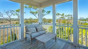 Eine überdachte Veranda mit einer hölzernen Bank und einer Couch, die einen Blick auf eine natürliche Landschaft mit Bäumen und offenen Feldern bietet.