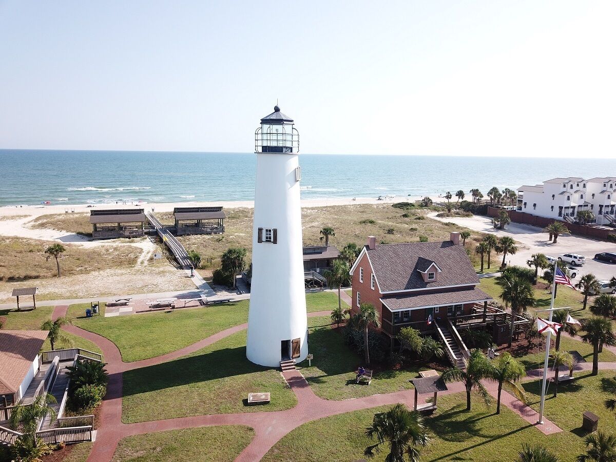 Un faro con una torre blanca y un edificio de techo rojo cercano.