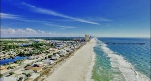 A coastal town with a long beach, a pier extending into the sea, and a dense cluster of buildings along the shore.