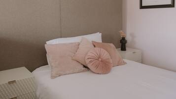 Un dormitorio ordenado con cama, almohadas, una mesita de noche y un dibujo arquitectónico enmarcado en la pared.