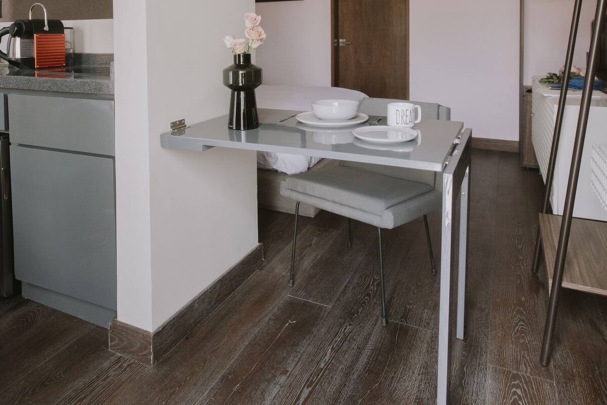 A modern kitchen with a built-in oven, a coffee machine, and a small dining area with a table and chairs.