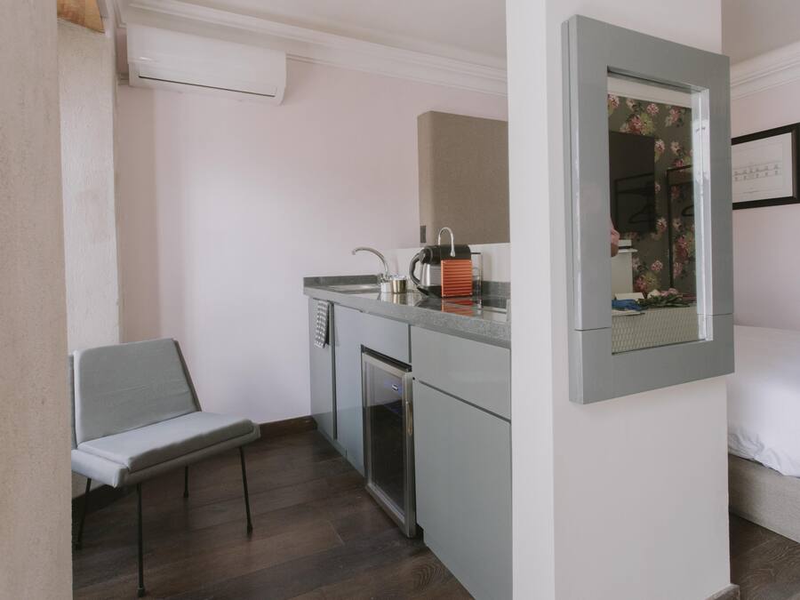 Una kitchenette compacta con un lavabo, un refrigerador pequeño y un microondas. Incluye una banca y una cama con ropa blanca.