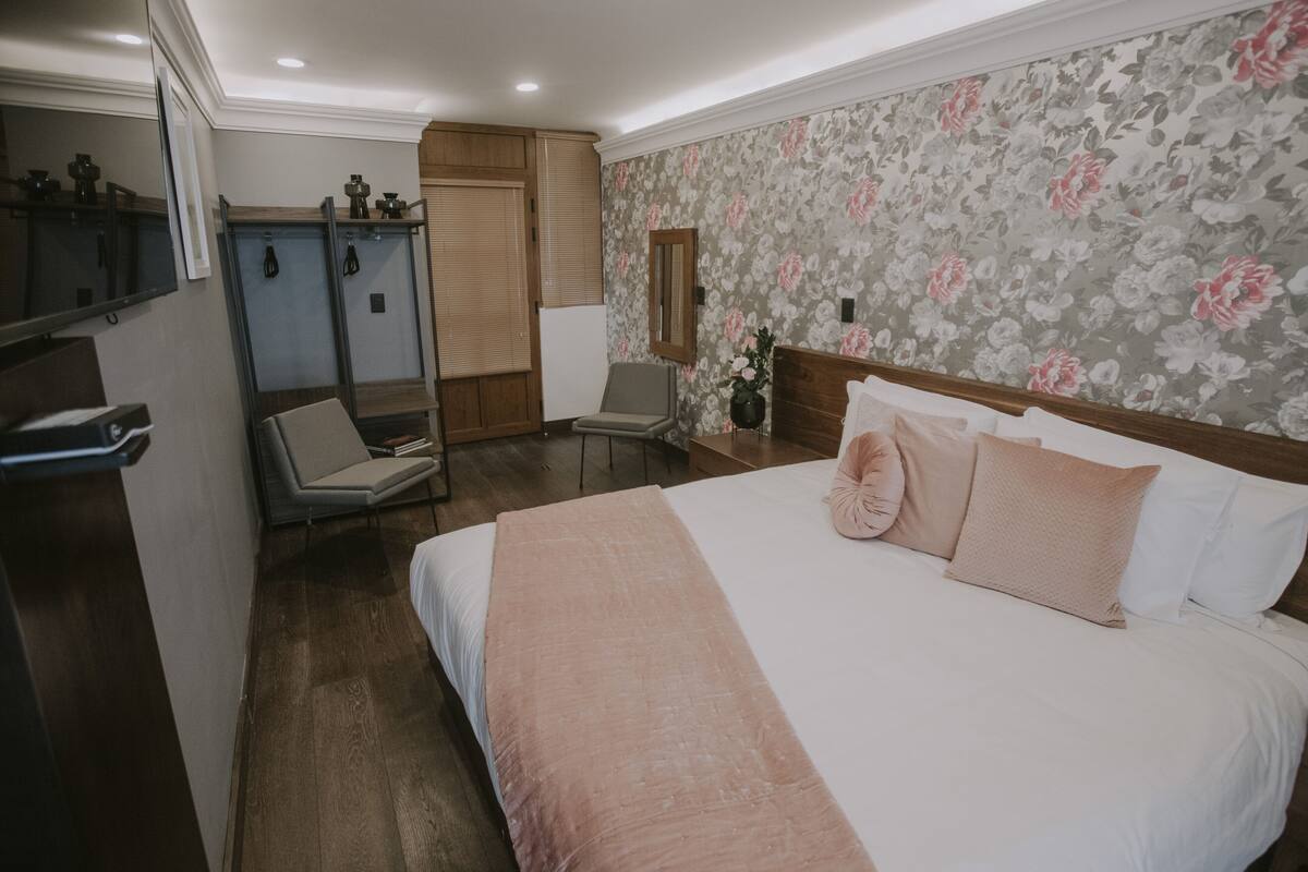 A bedroom with a large bed, a chair, a vanity with a mirror, and a wardrobe.