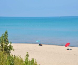 Een strand met een zandrijk strand, een paar mensen en een rode parasol.
