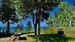 Nurmikkoalueella, jossa on puita, sijaitsee piknikpöytä ja penkki, ja sieltä on esteetön näkymä vesistöön.
