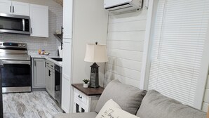 A compact kitchen with white cabinetry, a microwave, stove, and an air conditioning unit. - Crossroads to Pickwick Cabin SMOOTH SAILING (Iuka)