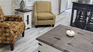 A cozy living room with a patterned armchair, a sofa, a coffee table with a pumpkin decoration, a clock, and a fish hanging on the wall. - Crossroads to Pickwick Cabin SMOOTH SAILING (Iuka)