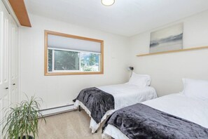 Quarto com duas camas, janela com vista para árvores, radiador e planta em vaso.