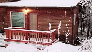 En stuga av trä med en röd veranda, en dörr och ett fönster.
