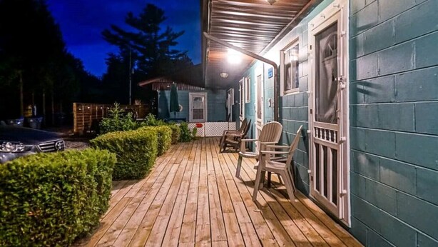 Una terraza de madera con sillas, un coche y un edificio con paredes azul turquesa y un porche.