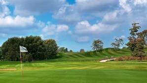 Campo de golf con un mástil de bandera, árboles y colinas onduladas.