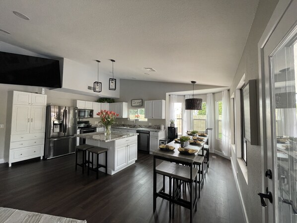 A modern kitchen with white cabinets, a stainless steel refrigerator, a central island with stools, and pendant lighting.