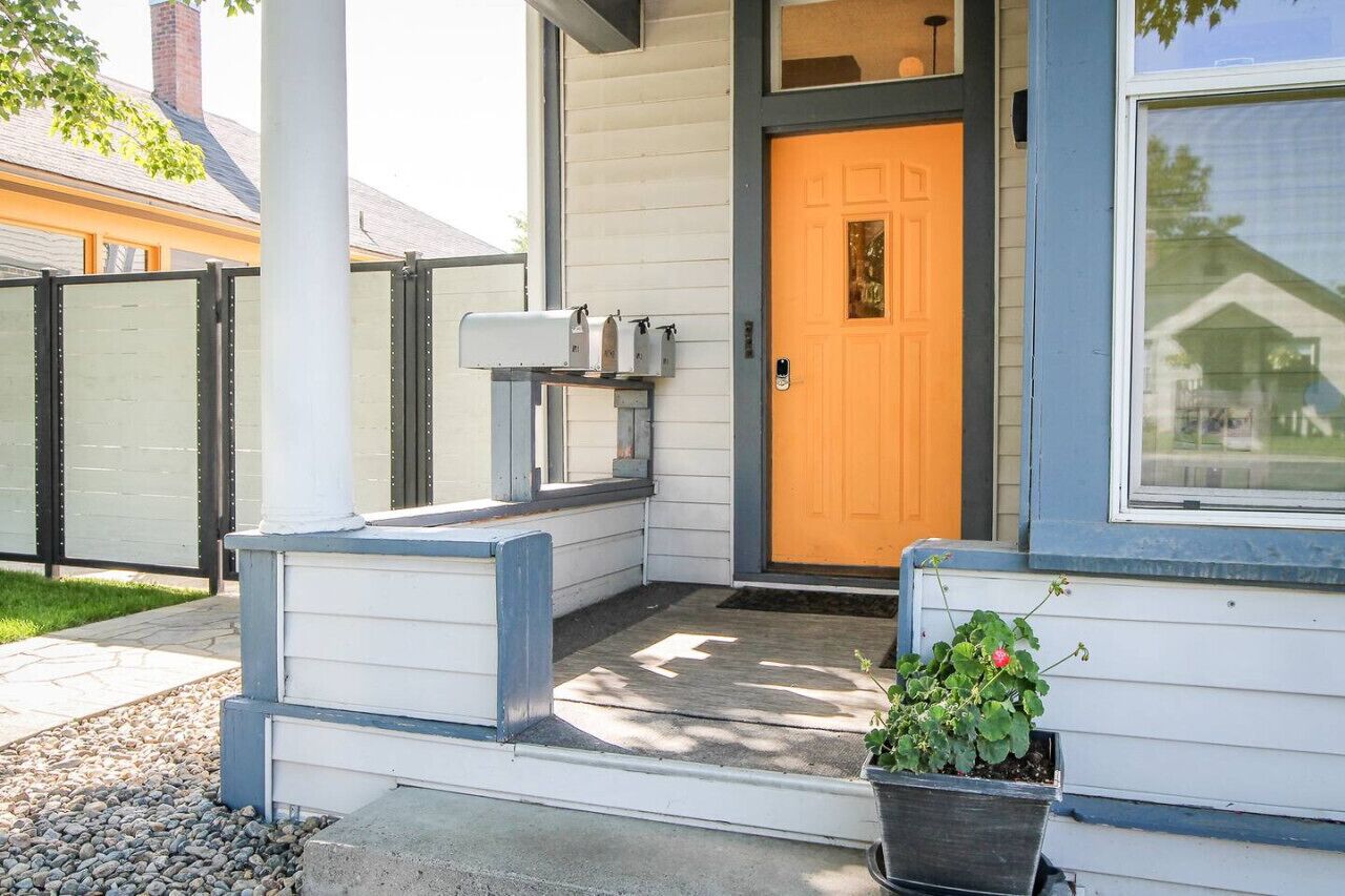 A house with a yellow front door, a mailbox, and a potted plant on the porch.