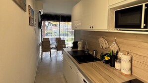 Moderni keittiö, jossa on valkoiset kaapit, musta työtaso, mikroaaltouuni, astianpesukone ja pesuallas. Viereisessä ruokailutilassa on tuoleja ja pöytä.