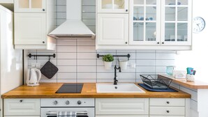Une cuisine moderne avec des armoires blanches, un plan de travail en bois, un four encastré et une bouilloire noire.