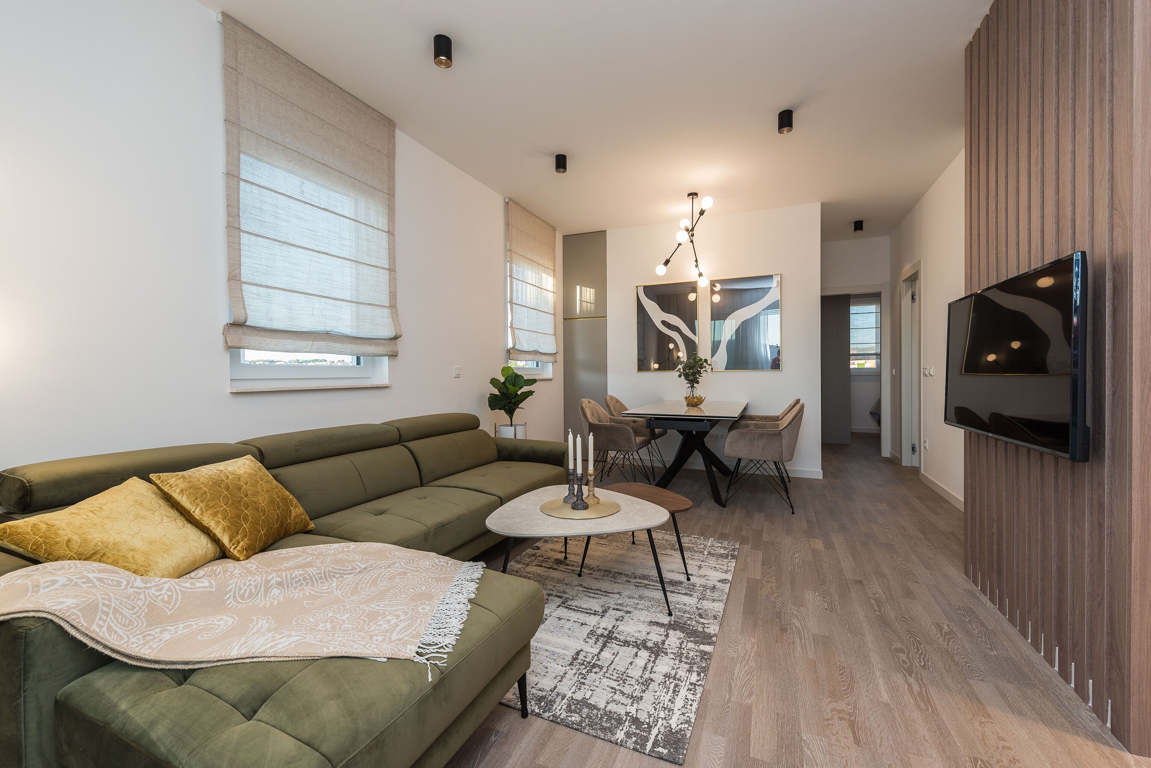 A modern living room with a green sofa, a small round table, and a TV mounted on the wall.