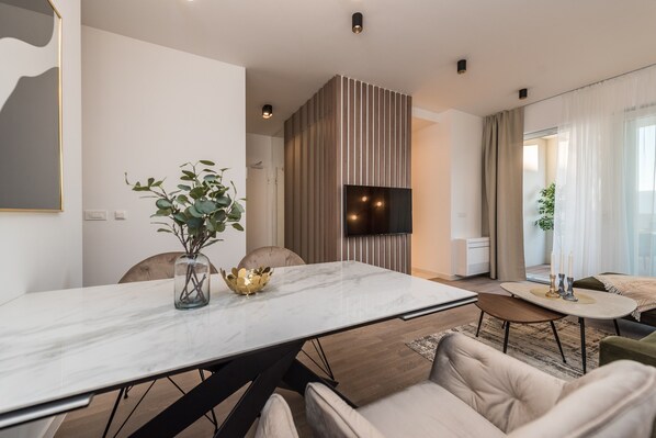 Un salon moderne avec une grande table en marbre blanc, un canapé confortable et un téléviseur à écran plat fixé sur un mur recouvert de panneaux en bois.