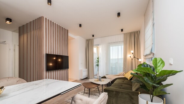 A modern living room with a flat-screen TV mounted on a wooden panel, a dining area with a marble table, and a green sofa. - Two Bedroom Apartment with Terrace (Zadar)
