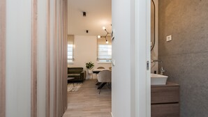 A modern interior with a wooden floor, a green sofa, a dining area with a table and chairs, and a bathroom with a sink and mirror. - Two Bedroom Apartment with Terrace (Zadar)