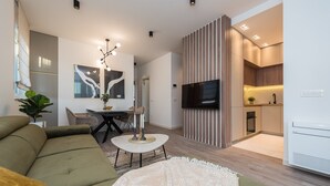 A modern living room with a sofa, a coffee table, and a TV. There is a kitchen area with a stove and a refrigerator. - Two Bedroom Apartment with Terrace (Zadar)