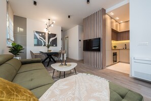 Un salon moderne avec un canapé, une table basse et un téléviseur. Il y a également un coin cuisine équipé d’une cuisinière et d’un réfrigérateur.