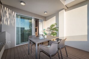 Un balcon avec une table et des chaises en bois, une plante en pot et une porte vitrée donnant sur un espace intérieur.