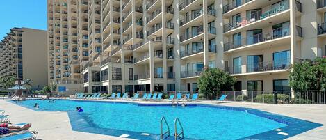 Uma piscina grande com espreguiçadeiras e um arranha-céu ao fundo.