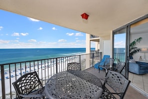 Un balcon avec vue sur la plage et l’océan, comprenant une table et des chaises, un canapé bleu et une plante en pot.